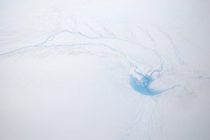 An example of a supraglacial lake and rivers on the surface of the Greenland Ice Sheet. The water flows down a hole (a moulin) in to the ice sheet in the center right. Photo by Thomas Nylen.