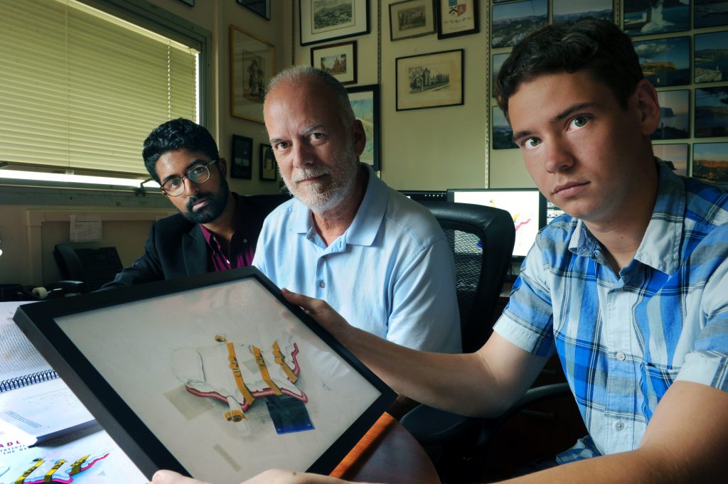 From left, Arvind Krishnamurthy, Frank Baumgartner and Justin Cole, who all worked on the book, "Deadly Justice." Cole is holding a copy of the original artwork for the book cover, which was created by Cerron T. Hooks, an inmate on North Carolina's Death Row. (photo by Donn Young)